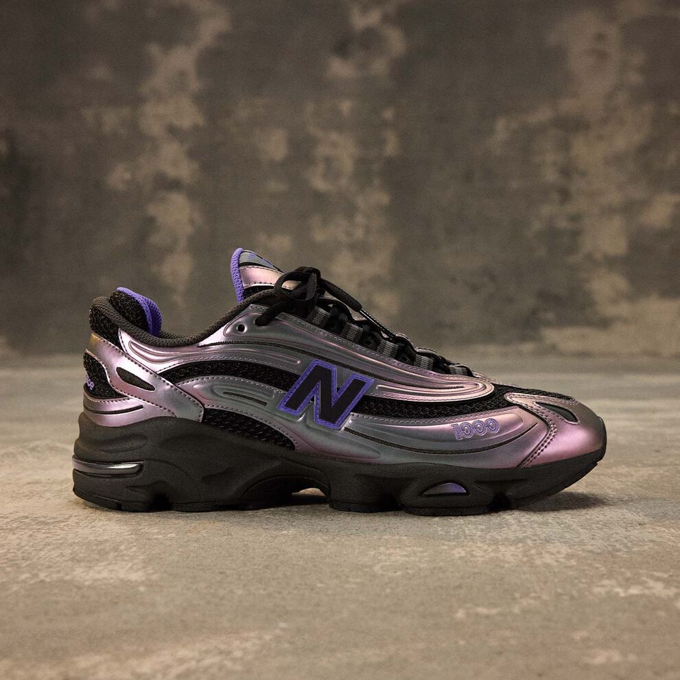 The 1000 New Balance shoe shot from the side behind a brown studio backdrop. 